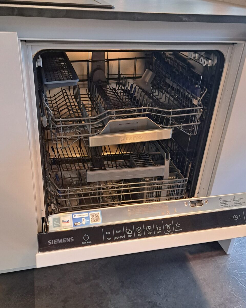 Ein moderner Siemens-Geschirrspüler mit geöffneter Tür, die leere Einschübe und ein Spülmittelfach zeigt. Das Bedienfeld mit Tasten und Digitalanzeige ist an der Vorderkante der Tür sichtbar.