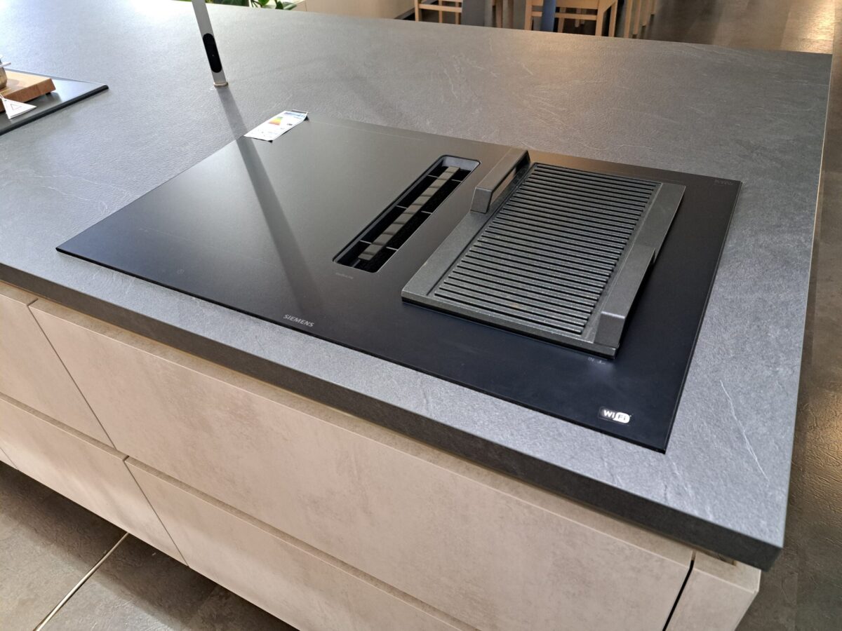 Ein modernes schwarzes Siemens Induktionskochfeld mit integriertem Lüftungssystem und Grillplatte ist auf einer grauen Kücheninsel mit hellen Schubladen installiert. Die Arbeitsplatte hat eine glatte, matte Oberfläche.