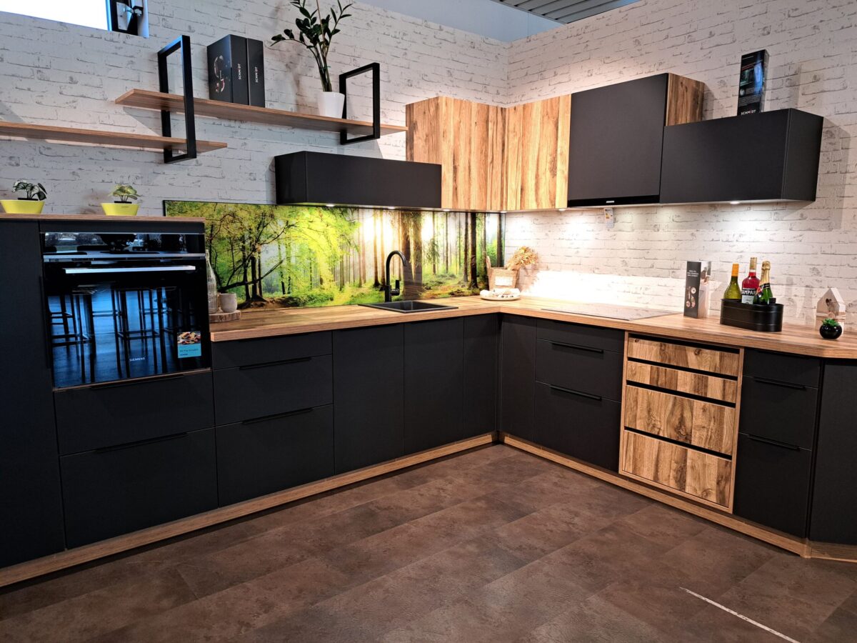 Moderne Küche mit Fronten in matt-schwarz und Holz, eingebautem Backofen, offenen Regalen und einer Nischenrückwand im Walddesign. Weiße Backsteinwände und Topfpflanzen sorgen für einen natürlichen Touch, während Unterbauleuchten den Arbeitsbereich erhellen.