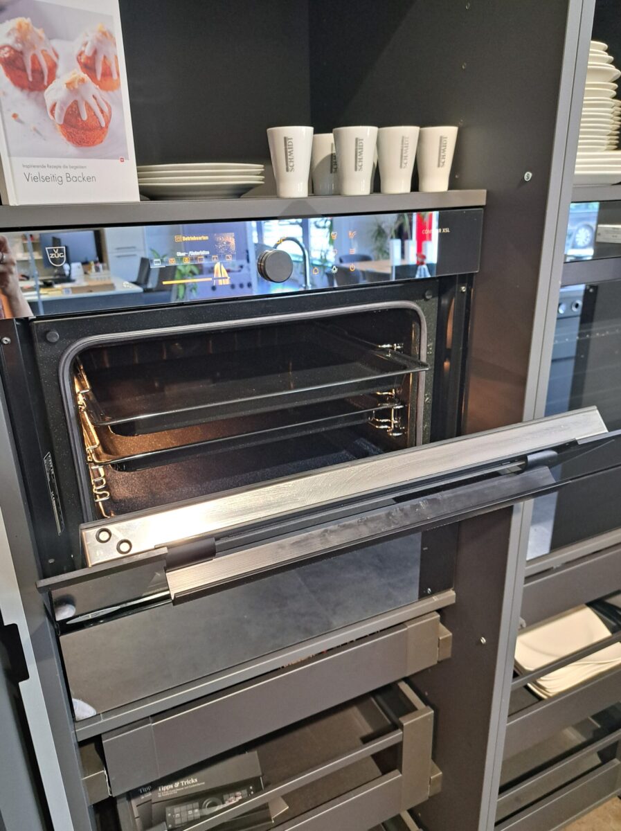 Ein CombAir Backofen von VZUG zum Einbau mit geöffneter Tür, in der zwei Backauszüge zu sehen sind. Die Optik ist verspiegeltes Glas.